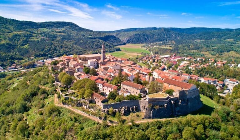 Buzet, Chorvatsko – panoramatický pohled na historické centrum města s kamennými domy a zelenými kopci v pozadí.